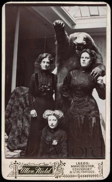Three women in Victorian dress pose for a photo with a bear