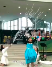 A little girl sings "Let It Go" from Frozen as two girls behind her throw silver streamers for a magic-snow effect